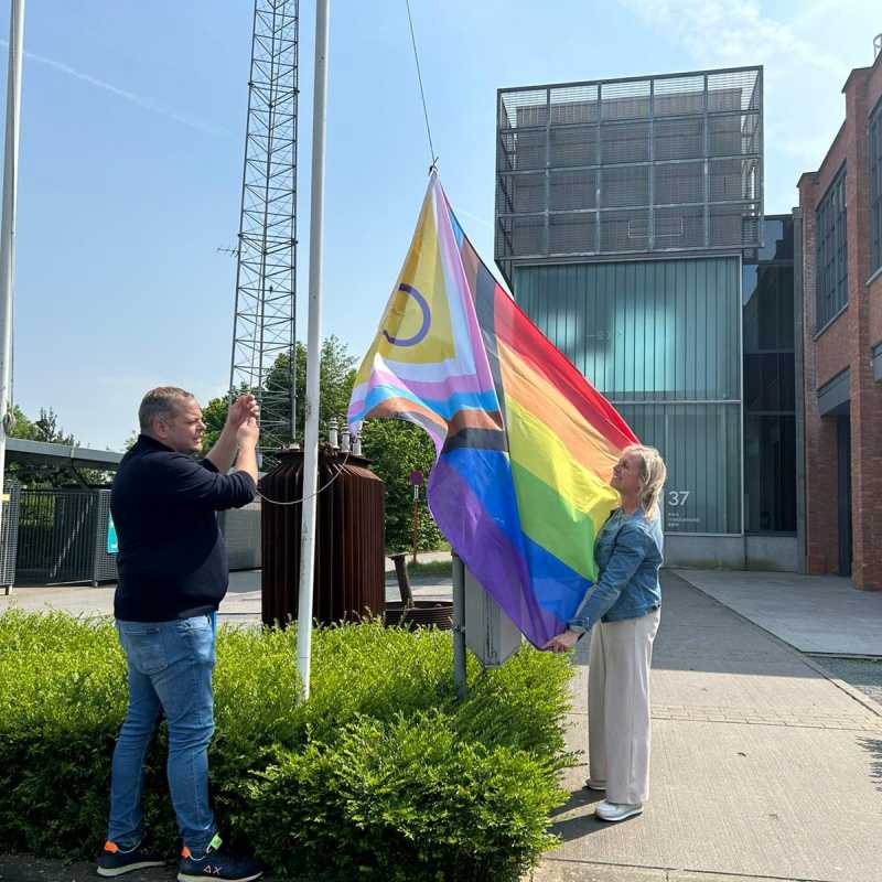 Schepen Benjamin Rogiers en schepen Hilde Van Impe hangen de nieuwe progress pride vlag op aan de Wattenfabriek. ©Lokaal Bestuur Herzele